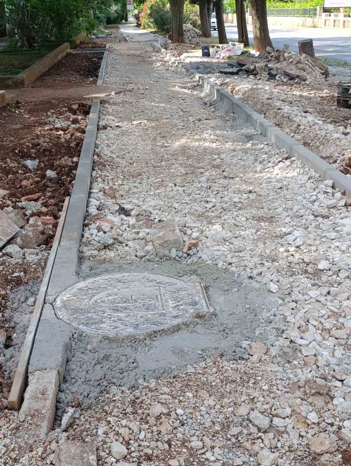 Novi šaht zaliven betonom na pješačkoj stazi, okolo razbacana šuta