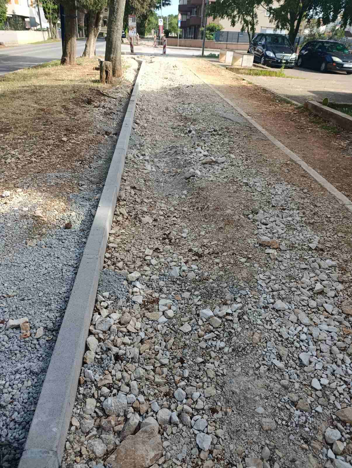 Pješačka staza između rubnjaka prekrivena slojem krupnog kamena, neprohodna za kolica