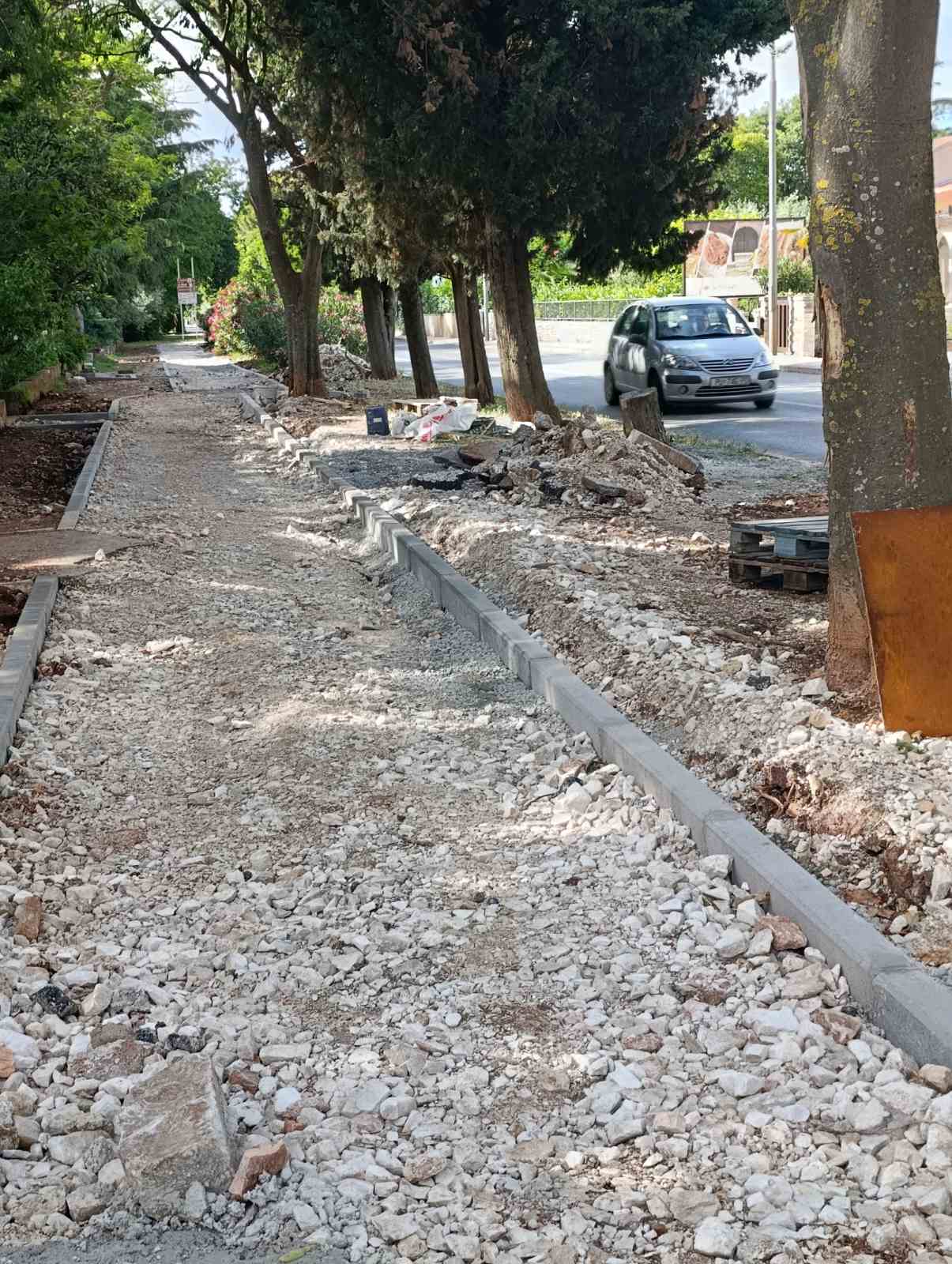 Staza uz cestu kod škole s razbacanim otpadom, kanisterima i najlonima
